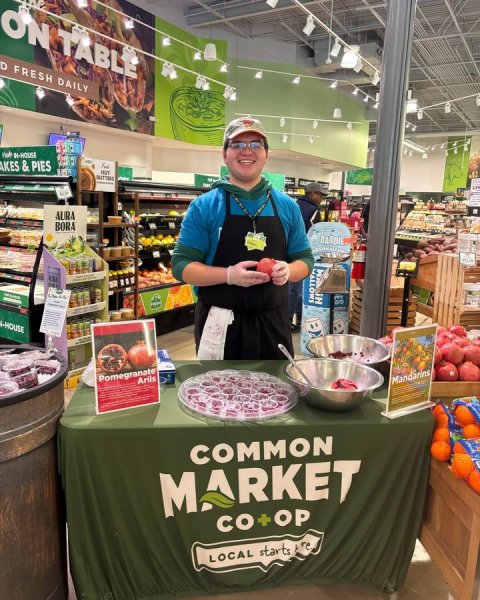 Adult, Man, Person. Text: ON TABLE D FRESH DAILY AKES &amp; PIES - AURA BORA SH ES Pomegranate Arils Mandarins COMMON MARKET