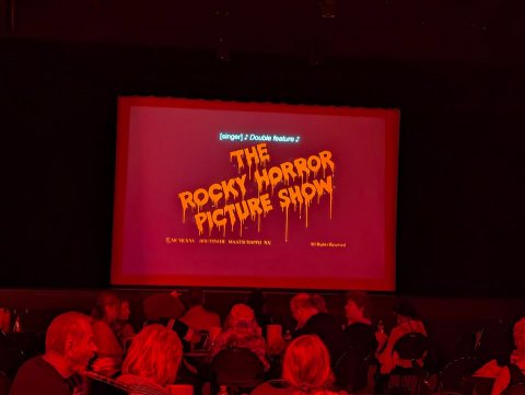 Cinema, Screen, Person. Text: THE ROCKY HORROR PICTURE SHOW